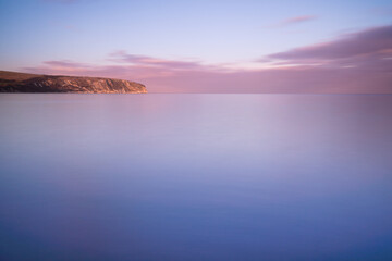 Fototapeta premium Slow shutter speed image of the sea and horizon as the sun sets in Swanage. Smooth calm ocean water with pink blue and purple colours at sunset in the UK