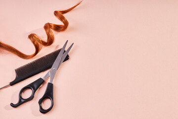 Red curly lock of hair, scissors and a comb on beige background with copy space
