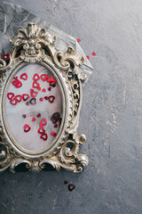 Obraz na płótnie Canvas A concrete gray background with a vintage silver photo frame, in which a photo of young people in love is inserted, next to it lies a scattering of red sequins in the shape of a heart.