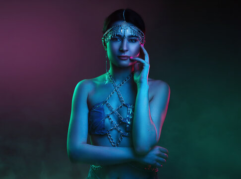 Portrait of a woman wearing fashionable luxury jewelry chains, in an oriental suit and diadem. Scheherazade's fairy tale in colorful bright neon blue and purple lights mystic smoke in the studio