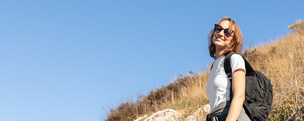 Young adult beautiful happy caucasian woman enjoy walking with backpack outdoors hill and mountain. Female tourist hiking outside at cliff staircase. Portrait smiling traveling active lady
