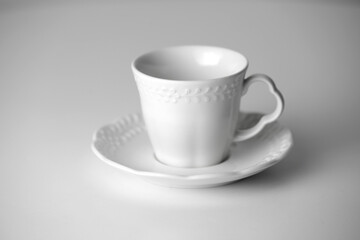 White tea cup and saucer with a pattern for drink on white background. Ceramic coffee cup or mug close up. Mockup classic porcelain utensils. copy space