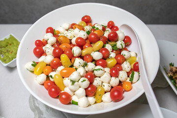 Italian tricolore, small balls of fresh white soft Italian mozzarella cheese, ripe red cherry tomatoes and fresh green basil herb, ready for making caprese salad, close up.