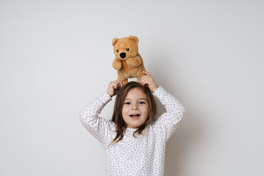 Young pretty caucasian girl with vintage teddy bear in pyjamas in white studio 