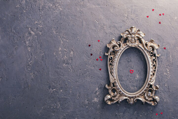 A concrete gray background with a vintage silver photo frame, in which a photo of young people in love is inserted, next to it lies a scattering of red sequins in the shape of a heart.