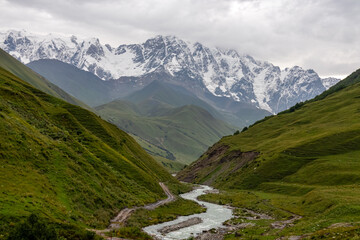 Patara Enguri River flowing down the a valley with view on the Shkhara Glacier in the Greater Caucasus Mountain Range in Georgia, Svaneti Region, Ushguli. Snow-capped mountains in the back. Wilderness