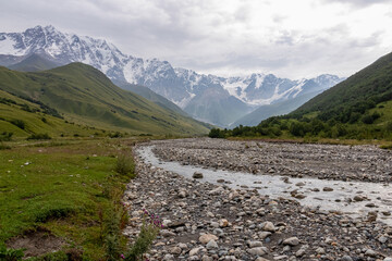 Naklejka premium Patara Enguri River flowing down the a valley with view on the Shkhara Glacier in the Greater Caucasus Mountain Range in Georgia, Svaneti Region, Ushguli. Snow-capped mountains in the back. Wilderness