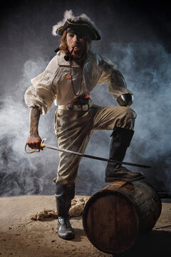Pirate filibuster sea robber in suit with saber is standing next to barrel. Concept photo