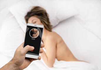 Male hand holding smartphone with husband incoming call on the background of naked unfaithful woman