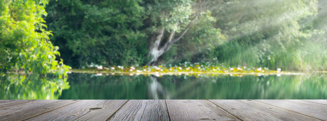 empty wooden jetty planks in front of a blurred water idyll background with wild vegetation in...