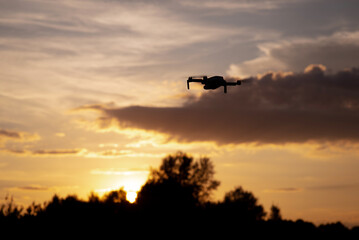 Fototapeta na wymiar Silhouette of drone flying in the sky and filming sunset. Small portable aircraft in flight
