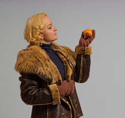 woman in a winter fur jacket with an orange in her hand on a white background, close-up