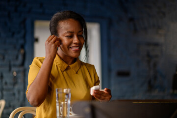 African american woman using airpods and a smartphone while sitting in a cafe