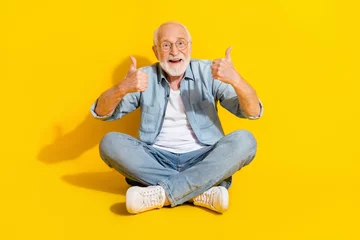 Zelfklevend Fotobehang Portrait of attractive cheerful grey-haired man sitting lotus position showing thumbup isolated over bright yellow color background © deagreez