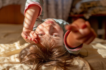 Happy beautiful girl in pajamas lying on back and getting up or waking up in the sunny ​morning.