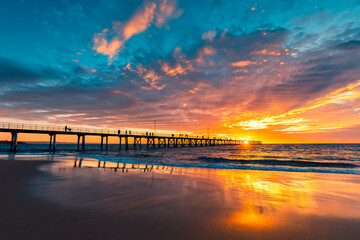Dramatic sunset viewed towards Port Noarlunga jetty with people strolling along, South Australia