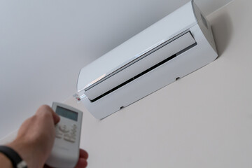 a man's hand holds the remote control of a wall-mounted conditioner
