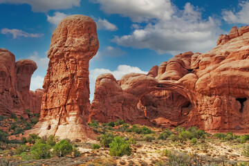 View on funny eroded red rugged sandstone formation with stone pillar and natural arch in dry...