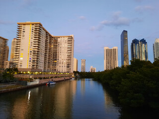 Sunny Isles, USA - March 22, 2021: high-rise buildings and green trees along river on blue sky