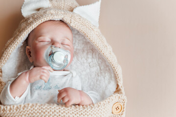 Reborn a boy doll with a pacifier sleeps in a knitted beige envelope. Copy space