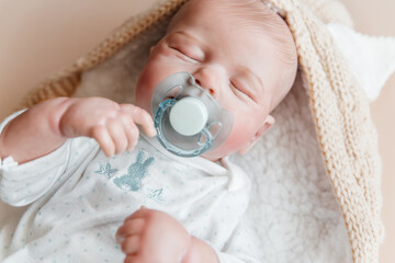 Reborn a boy doll with a pacifier sleeps in a knitted beige envelope. Close-up.