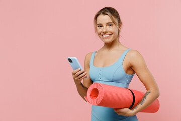 Young fun strong sporty athletic fitness trainer instructor woman wear blue tracksuit spend time in home gym hold use mobile cell phone isolated on pastel plain pink background. Workout sport concept.