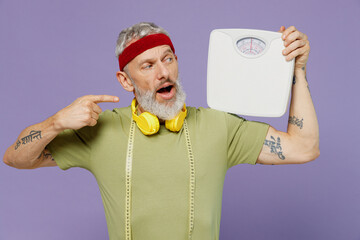 Elderly gray-haired bearded man 40s years old in headband khaki t-shirt hold look at floor scales...