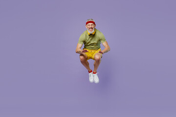 Full size body length vivid sporty elderly gray-haired bearded man 40s years old in headband khaki t-shirt jump touch hands with knees isolated on plain pastel light purple background studio portrait.