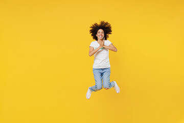 Fototapeta na wymiar Full body overjoyed young woman of African American ethnicity wears white volunteer t-shirt jump high hold face isolated on plain yellow background. Voluntary free work assistance help grace concept.