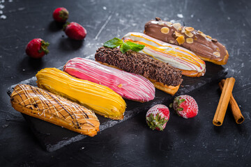 on a wooden cutting kitchen board, homemade food, black slate plate, colorful eclairs with berries,...