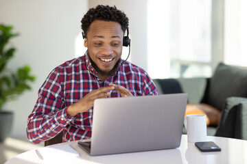 Black man at home remote working on laptop computer talking to his colleague