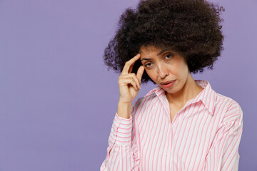 Young minded puzzled sad pensive woman of African American ethnicity 20s wearing pink striped shirt prop up head forehead look camera isolated on plain pastel light purple background studio portrait.