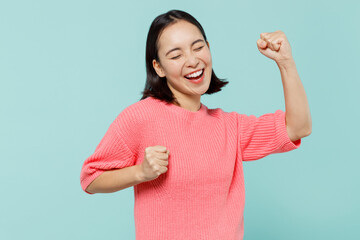 Young overjoyed happy excited woman of Asian ethnicity 20s wear pink sweater do winner gesture celebrate clenching fists say yes isolated on pastel plain light blue color background studio portrait - obrazy, fototapety, plakaty