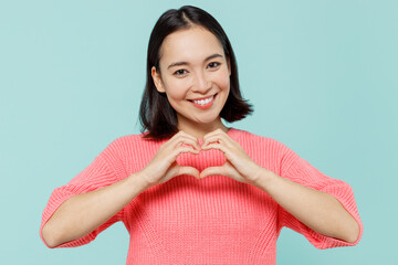 Young smiling happy woman of Asian ethnicity 20s in pink sweater showing shape heart with hands...