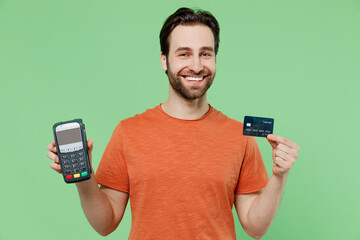 Young fun man 20s wear casual orange t-shirt hold wireless modern bank payment terminal to process acquire credit card payments isolated on plain pastel light green color background studio portrait