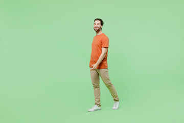 Full body side view smiling happy young man 20s wearing casual orange t-shirt walking going...