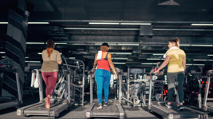 Back of multiethnic girls run on treadmill in gym