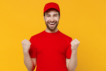 Naklejka premium Professional fun delivery guy employee man in red cap T-shirt uniform workwear work as dealer courier doing winner gesture celebrate clenching fists say yes isolated on plain yellow background studio.