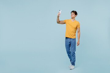 Full body young man 20s in yellow t-shirt doing selfie shot on mobile cell phone post photo on social network isolated on plain pastel light blue background studio portrait. People lifestyle concept - Powered by Adobe