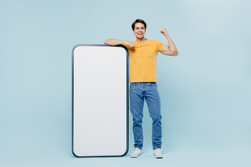 Full body young man in yellow t-shirt stand near mobile cell phone with blank screen workspace area...