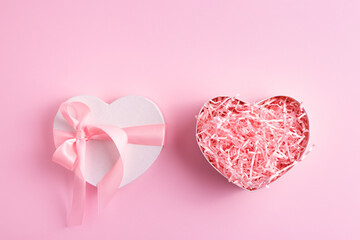 Festive heart shaped present box with pink shred paper on pastel pink background. Greeting, Valentine's day concept.