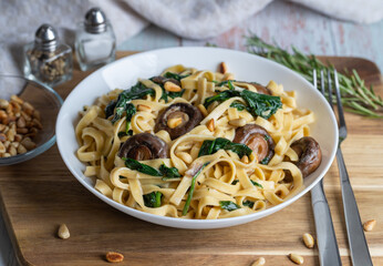 Rustic pasta with mushrooms, creamy spinach sauce and parsley on a wooden background