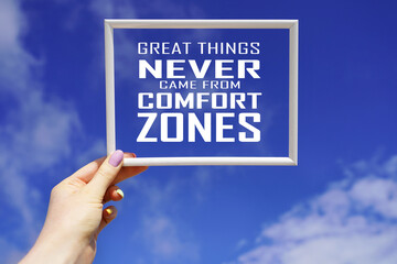 Great things never came from comfort zones. White frame in female hand with motivational words...