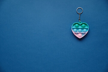 Keychain Heart, silicone colorful anti-stress toy on blue background. Click pop up bubble. A simple toy with dimples