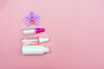 flat lay with cosmetic bottles and orchid flower on pink background with copy space for text. Top view cream jars set. The concept of face and body care.