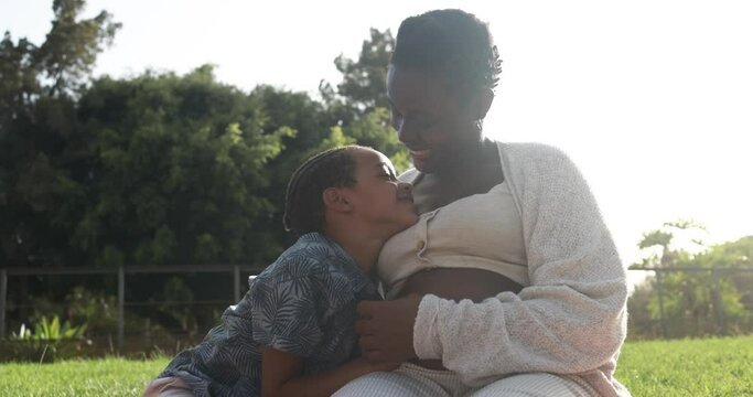 Happy african pregnant mother having tender moment with son at park