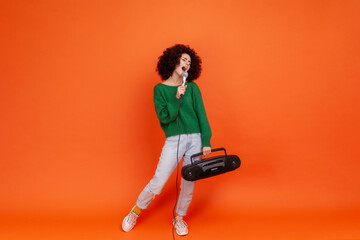 Full length portrait of woman with Afro hairstyle wearing green casual style sweater standing with...