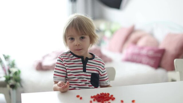 Cute little child, toddler boy, eating alfa omega 3 child suplement vitamin pills at home for better imunity