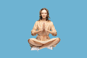 Hovering in air. Peaceful calm relaxed girl yellow dress levitating with prayer gesture, keeping...