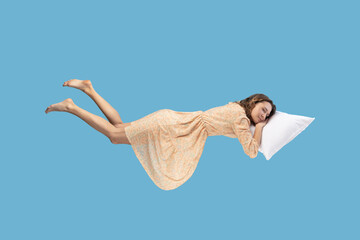 Relaxed girl in yellow dress levitating in mid-air, sleeping on stomach lying comfortable cozy on...